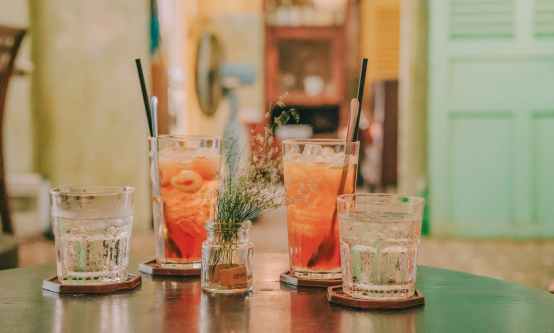 four clear glass drinking cups filled with orange and clear liquids on black surface
